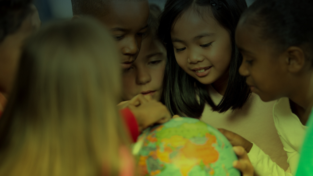 Grupo de crianças de diferentes etnias observa atentamente um globo terrestre em um ambiente escolar, simbolizando diversidade e interesse pelo mundo.