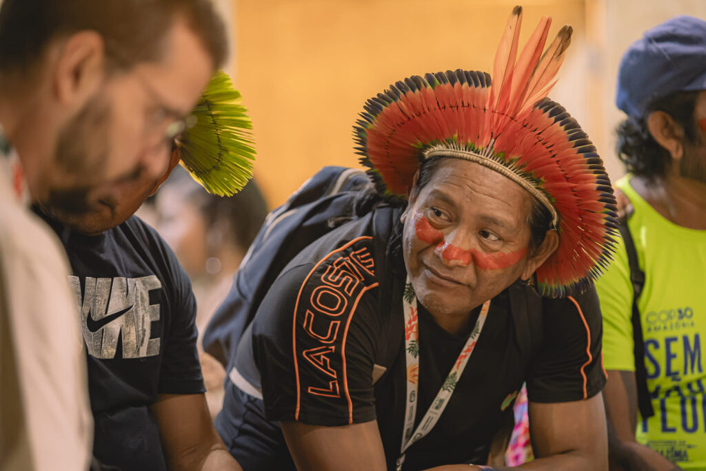 Liderança indígena com cocar tradicional e pintura facial vermelha participa de diálogo durante evento da COP30 Brasil Amazônia.
